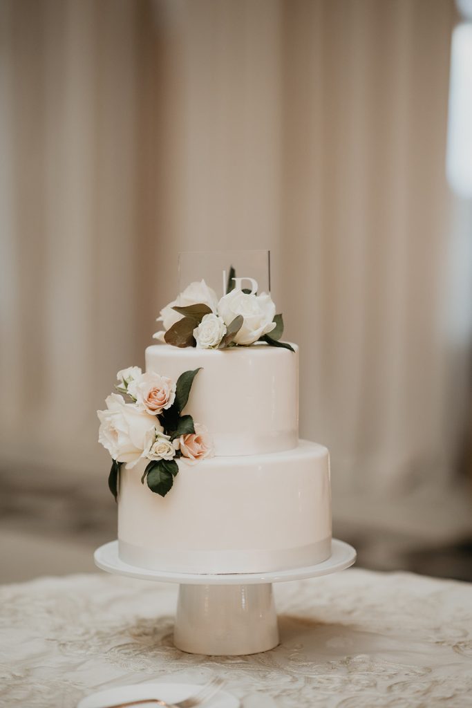 sleek white wedding cake with clear acrylic topper and white floral accents