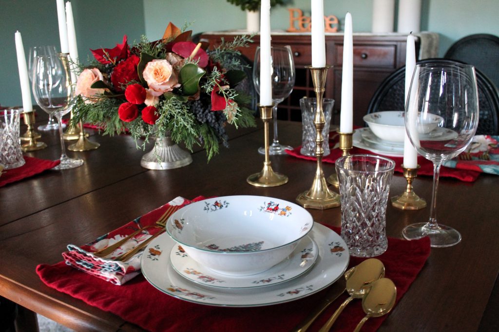 Christmas tablescape design with red placemats, floral napkins, Christmas dishware, gold flatware