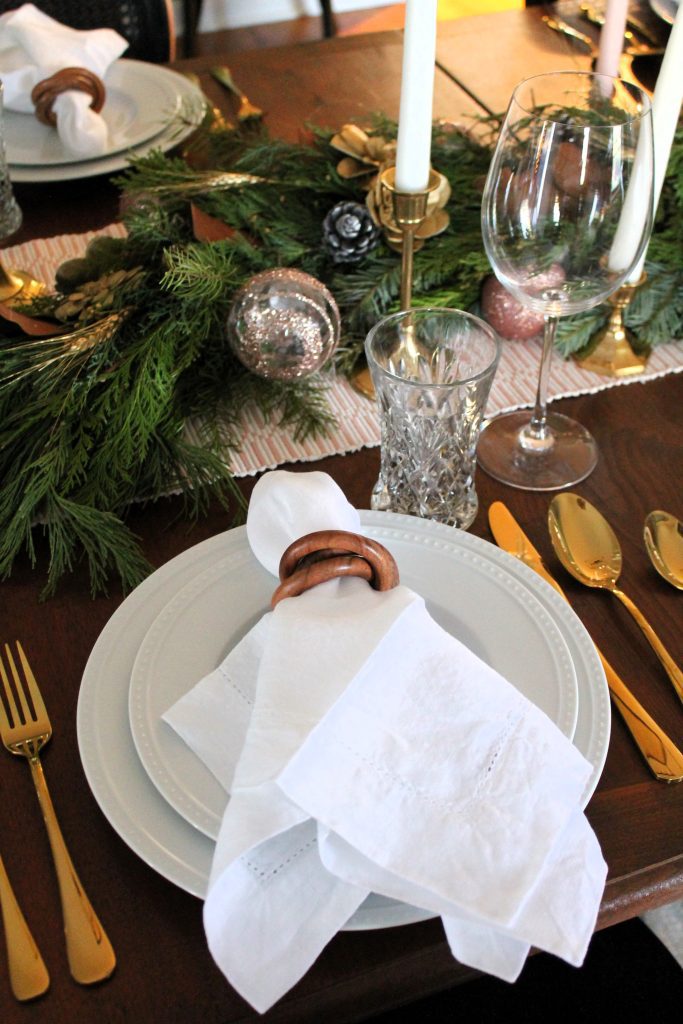 white dishware place setting with white linen napkin, wood bangles napkin ring, gold flatware